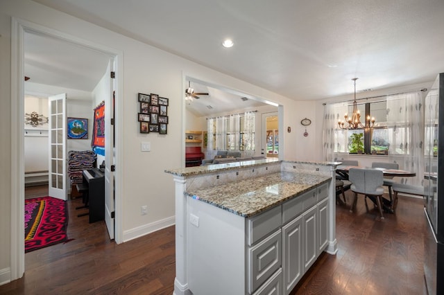 kitchen featuring baseboards, dark wood finished floors, a center island, light stone countertops, and an inviting chandelier