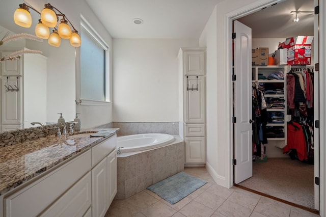 bathroom with a spacious closet, tile patterned flooring, a garden tub, and vanity