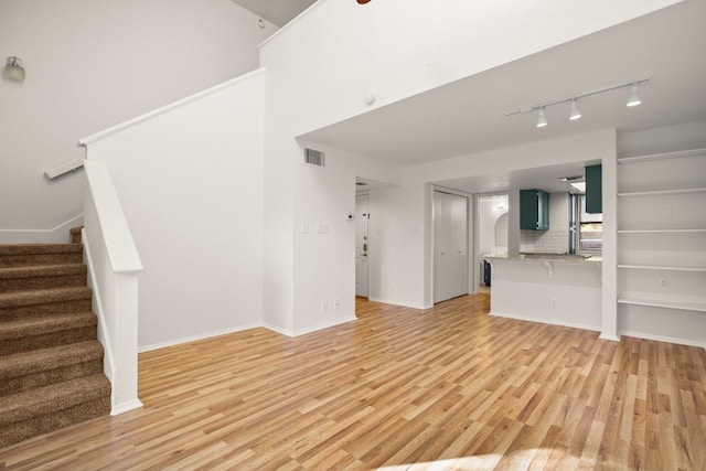 unfurnished living room with stairs, light wood-type flooring, visible vents, and baseboards