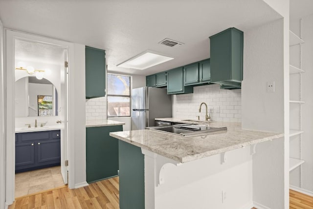 kitchen featuring a peninsula, visible vents, light wood-style floors, a kitchen breakfast bar, and freestanding refrigerator