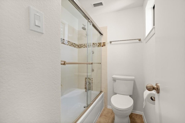 bathroom featuring toilet, combined bath / shower with glass door, visible vents, and baseboards