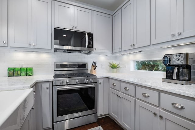 kitchen featuring stainless steel appliances, tasteful backsplash, dark wood-type flooring, and light stone counters