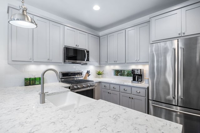 kitchen featuring appliances with stainless steel finishes, hanging light fixtures, gray cabinetry, and light stone countertops