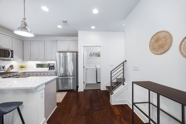 kitchen featuring stainless steel appliances, separate washer and dryer, a breakfast bar area, and decorative light fixtures