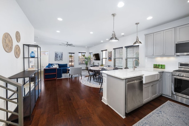 kitchen with light stone counters, open floor plan, a peninsula, stainless steel appliances, and a sink