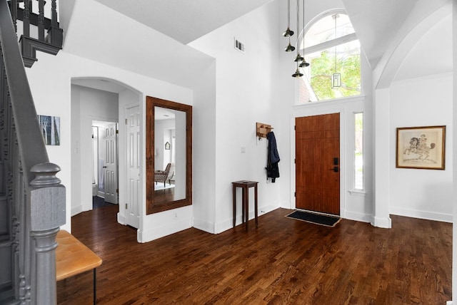 entrance foyer with visible vents, arched walkways, a towering ceiling, dark wood-style flooring, and stairs