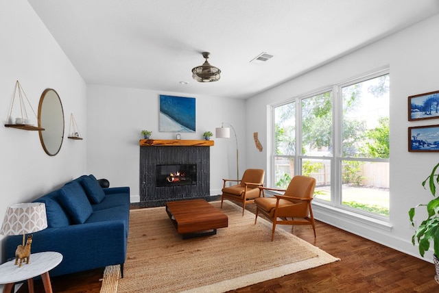 living area with baseboards, a fireplace with flush hearth, visible vents, and wood finished floors