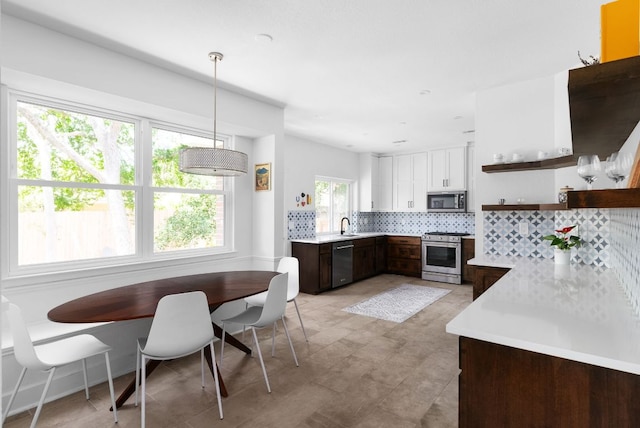 kitchen with appliances with stainless steel finishes, light countertops, white cabinetry, pendant lighting, and backsplash