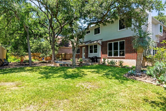 back of house with a yard, brick siding, and fence