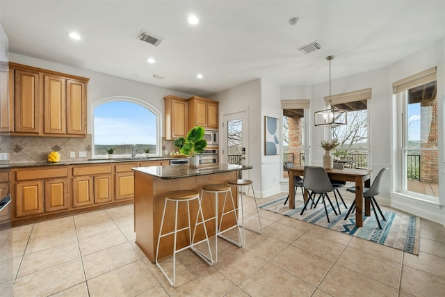 kitchen featuring a center island, decorative light fixtures, visible vents, a sink, and dark stone counters