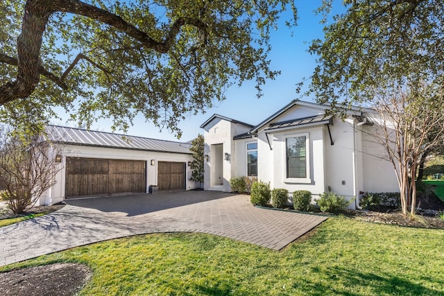 view of front of house with metal roof, an attached garage, decorative driveway, a front yard, and stucco siding