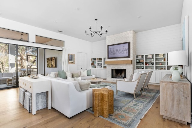 living room featuring light wood-style floors, a chandelier, visible vents, and a fireplace