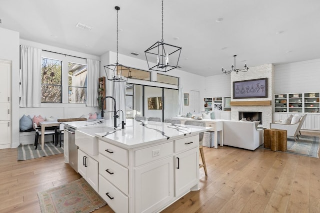 kitchen with a kitchen island with sink, white cabinets, open floor plan, light wood-type flooring, and pendant lighting