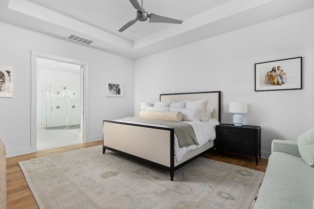 bedroom with baseboards, visible vents, connected bathroom, a raised ceiling, and wood finished floors