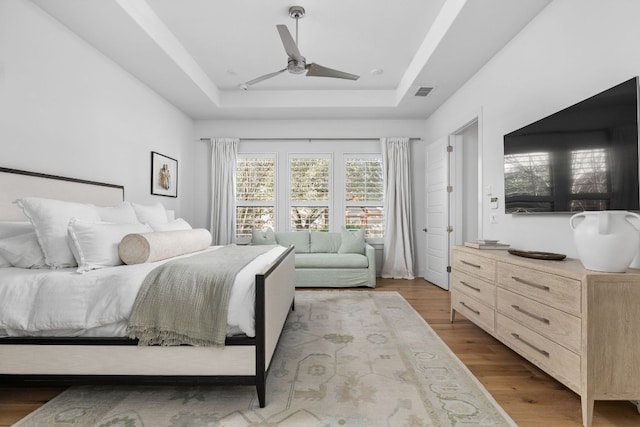 bedroom featuring a ceiling fan, visible vents, a raised ceiling, and wood finished floors