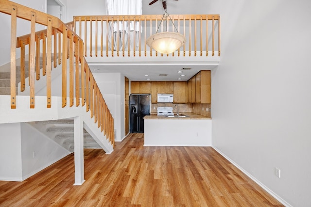 kitchen with white appliances, backsplash, a peninsula, light wood-type flooring, and a sink