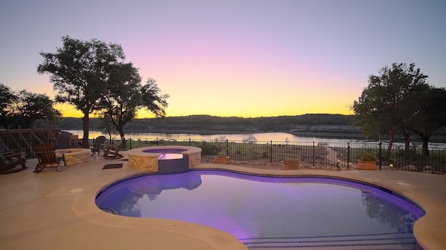 pool at dusk with a patio, a fire pit, a water view, fence, and a pool with connected hot tub