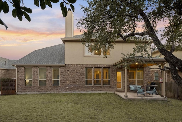 back of property at dusk featuring a patio, a lawn, fence, and stucco siding