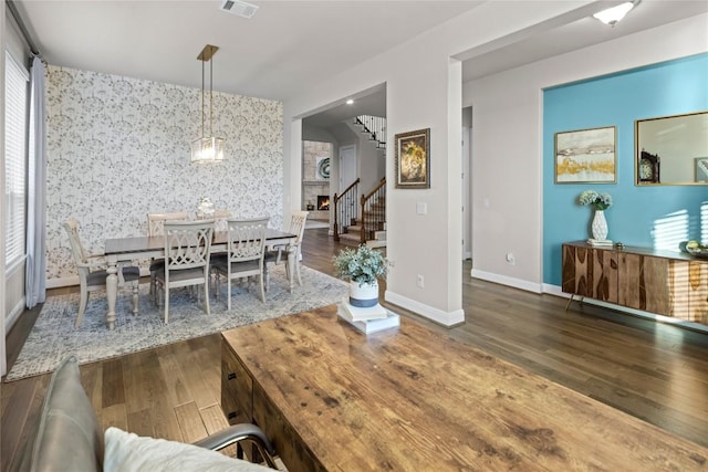 dining space featuring wallpapered walls, baseboards, visible vents, stairway, and wood finished floors