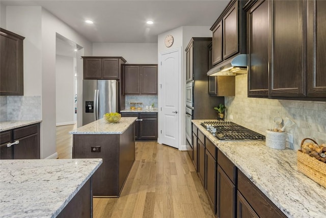 kitchen featuring light stone counters, under cabinet range hood, stainless steel appliances, dark brown cabinets, and light wood finished floors