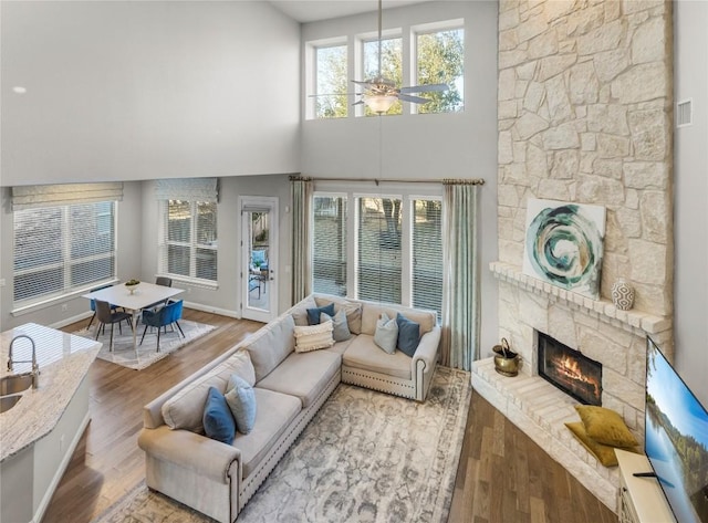 living room featuring ceiling fan, a high ceiling, a fireplace, and wood finished floors