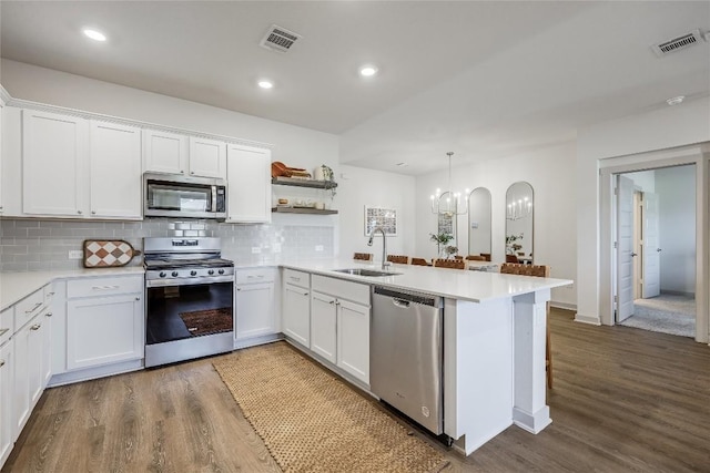 kitchen featuring visible vents, appliances with stainless steel finishes, a peninsula, open shelves, and a sink