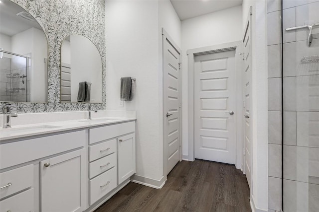 bathroom featuring double vanity, a shower stall, a sink, and wood finished floors