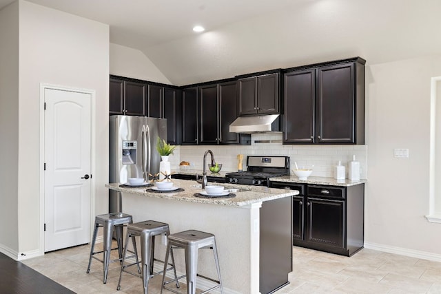 kitchen with lofted ceiling, decorative backsplash, appliances with stainless steel finishes, light stone countertops, and under cabinet range hood