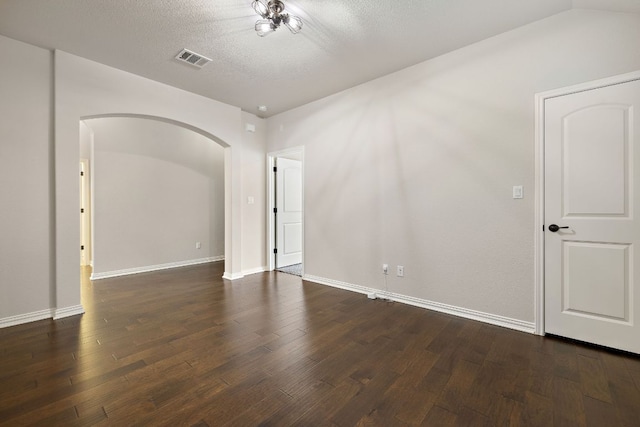 unfurnished room featuring baseboards, visible vents, arched walkways, dark wood-style floors, and a textured ceiling