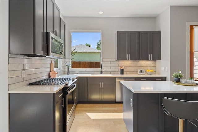 kitchen featuring stainless steel appliances, a sink, light countertops, light wood finished floors, and tasteful backsplash