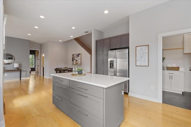 kitchen featuring light wood-type flooring, a kitchen island, stainless steel refrigerator with ice dispenser, and light countertops