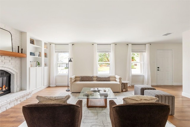 living area with a healthy amount of sunlight, a brick fireplace, light wood-style flooring, and visible vents