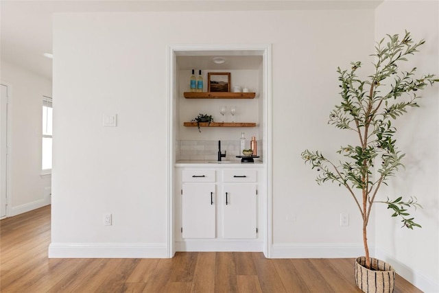 bar featuring decorative backsplash, light wood-style flooring, and baseboards