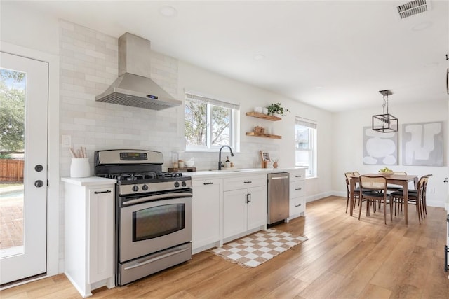 kitchen with visible vents, light wood-style floors, light countertops, appliances with stainless steel finishes, and wall chimney exhaust hood