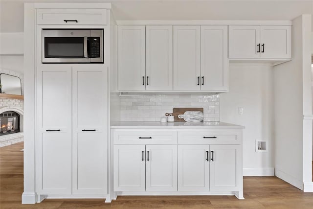 kitchen with light wood-style floors, stainless steel microwave, white cabinets, and light countertops