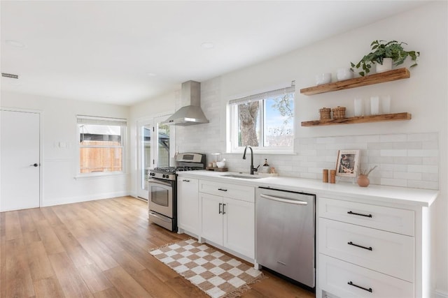 kitchen with stainless steel appliances, a sink, decorative backsplash, wall chimney exhaust hood, and light wood finished floors