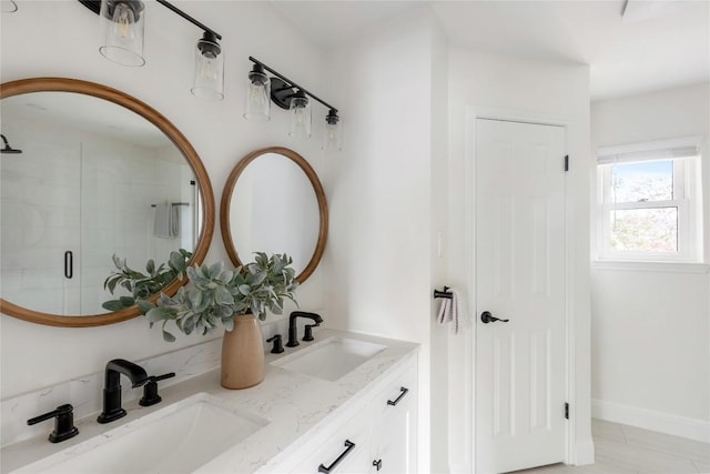 bathroom featuring double vanity, a stall shower, a sink, and baseboards