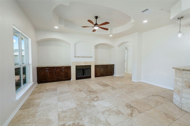 unfurnished living room featuring a tile fireplace, a raised ceiling, visible vents, and baseboards