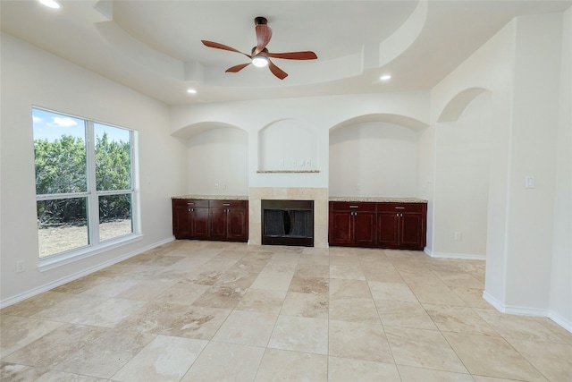 unfurnished living room featuring a fireplace, a raised ceiling, a ceiling fan, and baseboards