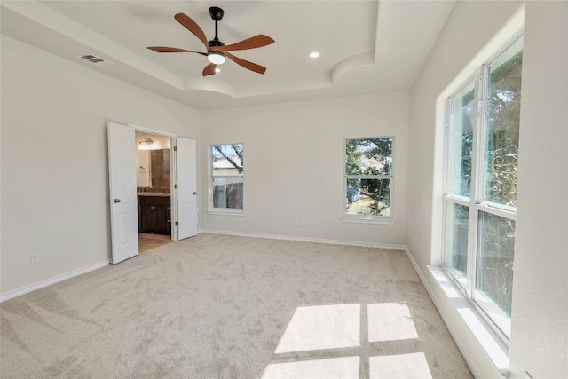 unfurnished bedroom with a tray ceiling, multiple windows, light colored carpet, and baseboards