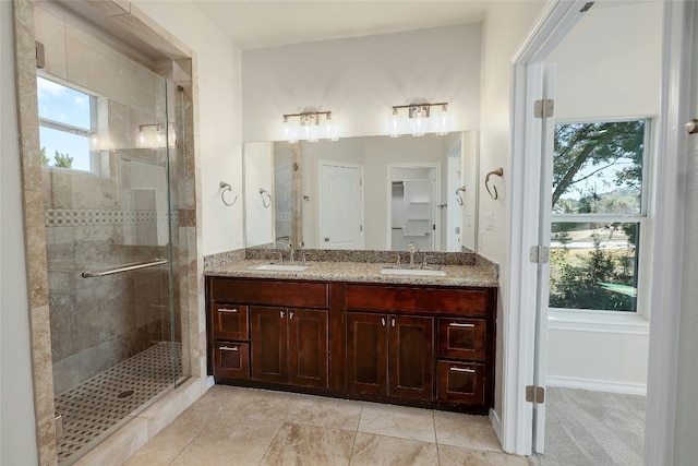 bathroom with double vanity, a shower stall, baseboards, and a sink