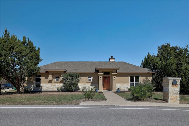 view of front facade with stone siding, a front yard, a chimney, and stucco siding