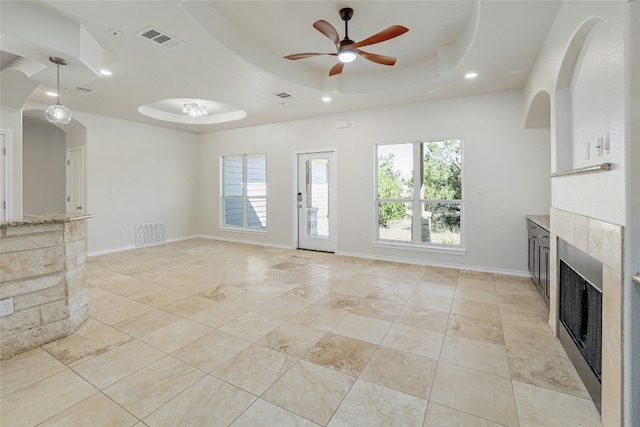 unfurnished living room with a tray ceiling, baseboards, visible vents, and a tiled fireplace