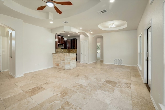 unfurnished living room featuring a tray ceiling, visible vents, and arched walkways