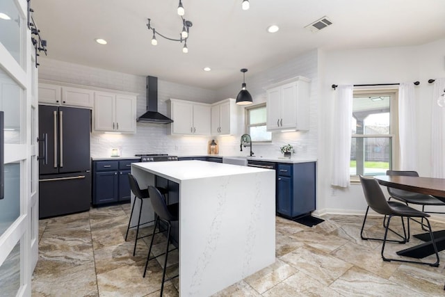 kitchen featuring high quality fridge, visible vents, light countertops, blue cabinetry, and wall chimney exhaust hood