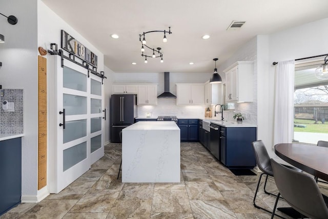 kitchen featuring a barn door, visible vents, stainless steel appliances, wall chimney range hood, and white cabinetry