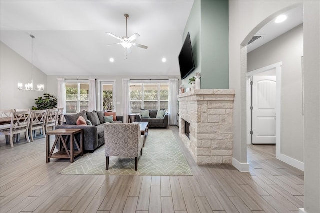 living area featuring baseboards, a stone fireplace, high vaulted ceiling, wood finish floors, and ceiling fan with notable chandelier