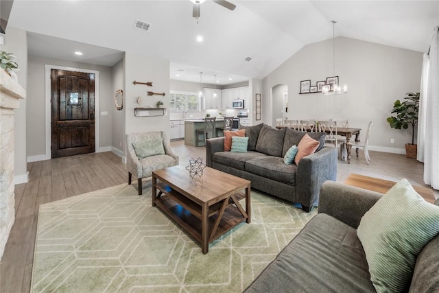 living room featuring arched walkways, visible vents, light wood-style flooring, vaulted ceiling, and baseboards