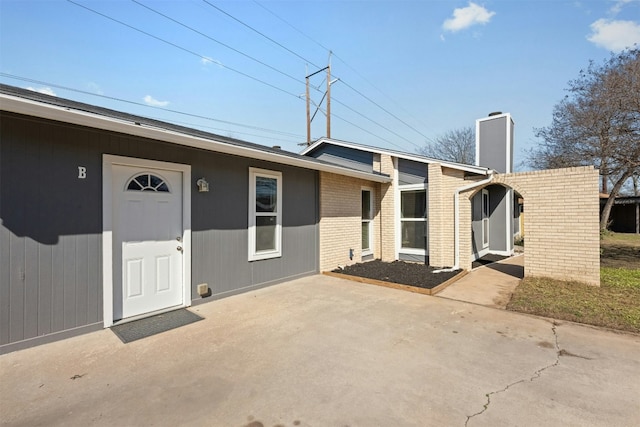 view of front of house featuring a patio, brick siding, and a chimney