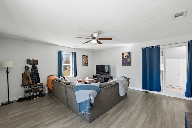 living room with visible vents, ceiling fan, light wood-style flooring, and baseboards